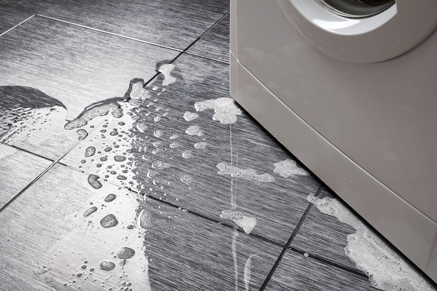 Top view a breakdown of a household washing machine. Water with foam out onto the tile floor from below.